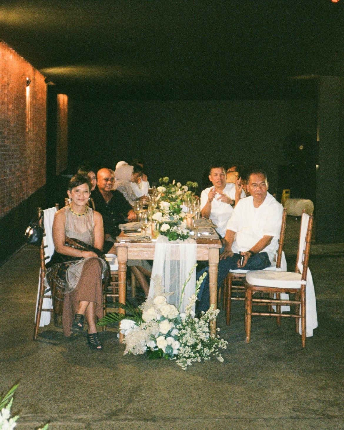 Wedding guests enjoying an intimate dinner at a decorated long table beside a signature red brick wall at Titik Dua Ubud