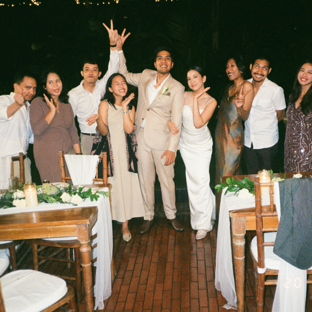 Wedding party and guests cheering and posing at an outdoor reception dinner