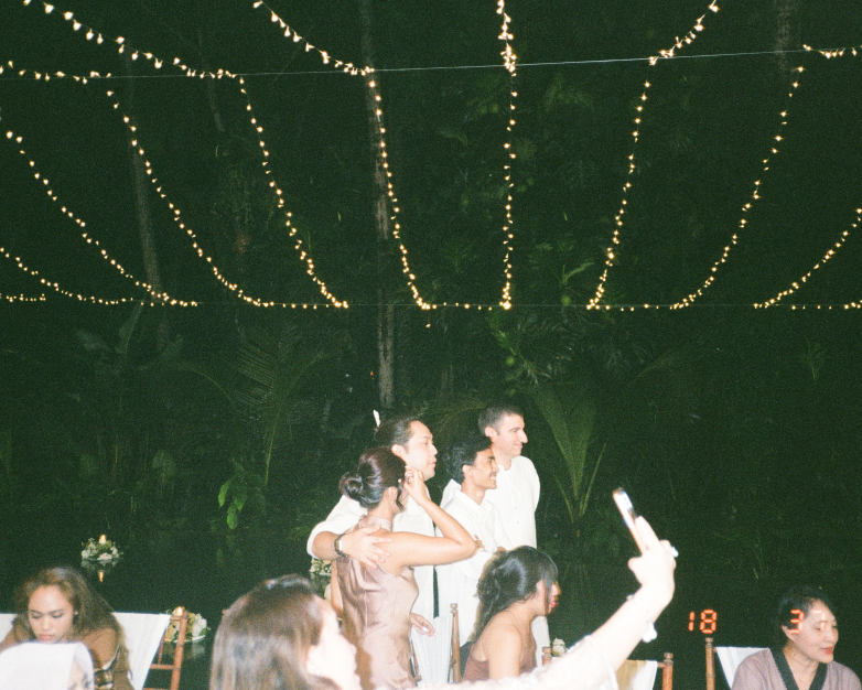 Night wedding celebration in Bali with guests taking photos under rows of warm string lights
