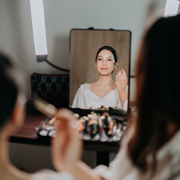 A bride getting her makeup done in a mirror during wedding preparations at Titik Dua Ubud